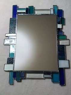 a mirror with blue and white glass pieces on it's sides, in the shape of a rectangle