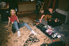 two people sitting on the floor with guitars and music equipment in front of them,