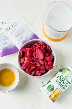 a bowl filled with red food next to a bag of yogurt and a cup of tea