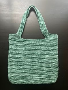 a green knitted bag sitting on top of a wooden table next to a cell phone