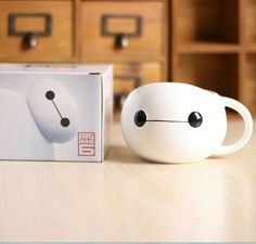 a white coffee cup sitting on top of a wooden table next to a cardboard box