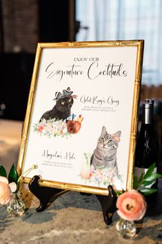 there is a sign with cats on it next to some wine bottles and flowers in the background