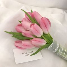 a bouquet of pink tulips sitting on top of a white sheet with a name tag