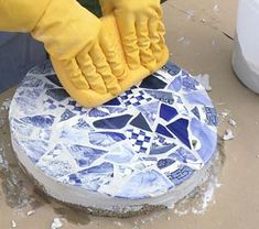 a person in yellow gloves is cleaning a blue and white mosaic tile surface with a rag