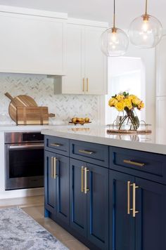 a kitchen with marble counter tops and blue cabinets, yellow flowers in vase on the island