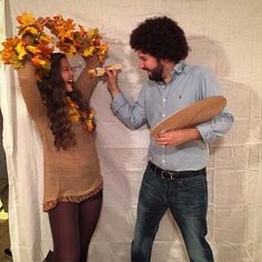 two people standing in front of a white backdrop eating pizza and talking to each other