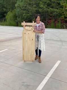 a woman standing next to a wooden object in a parking lot with trees in the background