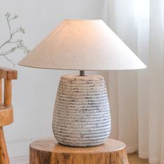 a table lamp sitting on top of a wooden stump in front of a white wall