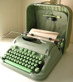 an old fashioned green typewriter sitting on top of a white table next to a suitcase