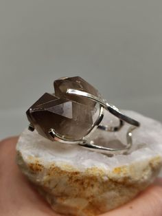 Elevate your elegance and give the gift of grounding with our Raw Smoky Quartz Ring. This exquisite piece showcases the natural beauty of smoky quartz, celebrated for its earthy hues and protective properties. It's not just a statement piece; it's a meaningful gift that captures the essence of strength and sophistication. 🔸Adjustable band ring  🔸20mm stone size 🔸Color may vary according to lighting 🔸 Silver filled We offer  🔸Fast shipping  🔸Free shipping (eligible orders) 🔸Polishing cloth Quartz Jewelry Ring Gift, Quartz Ring Jewelry For Gift, Silver Quartz Rings For Gifts, Smoky Quartz Gemstone Ring Jewelry, Silver Quartz Rings As A Gift, Silver Quartz Rings For Gift, Faceted Smoky Quartz Jewelry As Gift, Faceted Smoky Quartz Jewelry For Gift, Quartz Crystal Ring As A Gift