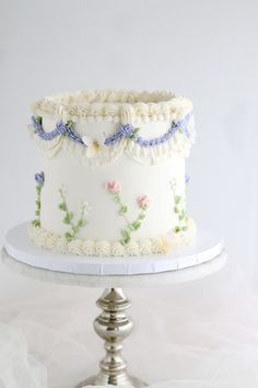 a white cake with flowers on it sitting on a silver platter next to a plate