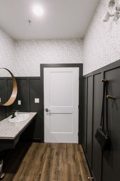 a bathroom with black and white walls, wood flooring and a round mirror on the wall