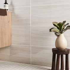 a white vase sitting on top of a wooden stool next to a wall mounted toilet