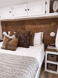 a bed with lots of pillows on top of it in front of white cupboards