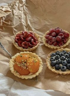 four pies with berries, blueberries and strawberries in them on a piece of wax paper