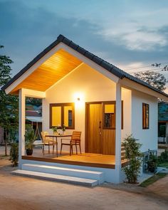 a small white house with a table and chairs on the front porch at night time