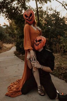 a man and woman dressed up as pumpkins sitting on the ground with their heads wrapped around each other