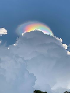 a rainbow appears in the sky above some clouds and trees on a sunny day with blue skies