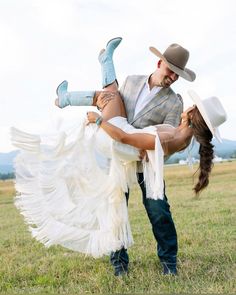 a man holding a woman in his arms while she is wearing a white dress and cowboy hat