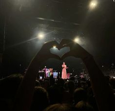 a person making a heart shape with their hands at a music concert in the dark