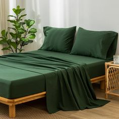 a bed with green sheets and pillows next to a potted plant on the floor