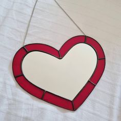 a red and white heart shaped mirror hanging from a chain on a white tablecloth