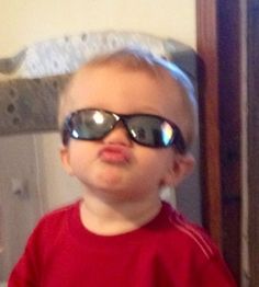 a little boy wearing sunglasses and making a funny face while standing in front of a mirror