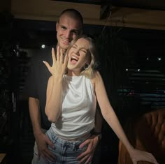 a man and woman standing next to each other in front of a chair with their hands on the face