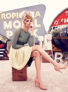 a woman sitting on top of a wooden bench in front of a neon motel sign