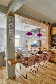 a dining room table and chairs in front of an open kitchen with brick walls, hardwood floors and exposed beams