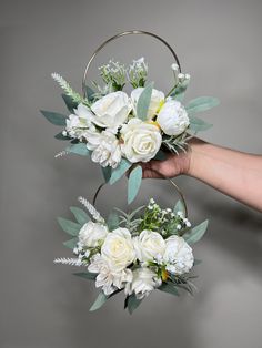 two white flowers and greenery are in the shape of hoop vases on a gray background