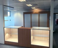 an empty office cubicle with glass shelves and sliding doors on both sides, in the middle of a large open space