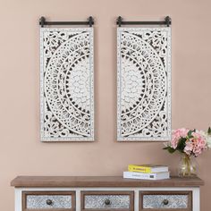 two white wall hangings on the side of a wooden table with drawers and flowers