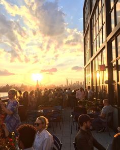 a group of people sitting at tables on top of a building with the sun setting in the background