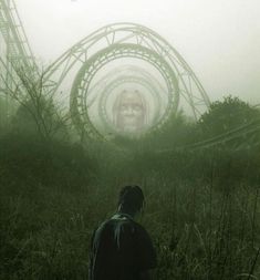 a man standing in front of a roller coaster on a foggy day at an amusement park