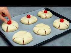 a person placing cherry tomatoes on top of buns in a baking pan with other pastries