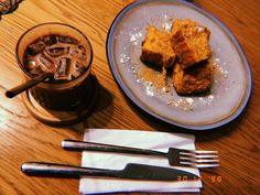 a plate with some food on top of it next to a fork and glass filled with liquid