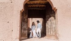 a man and woman are walking out of an adobe building with their wedding dress blowing in the wind