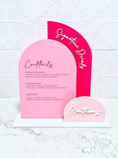 a pink and red wedding card with the word congratulations on it, sitting next to an arch shaped like a heart