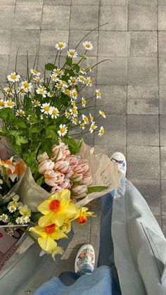 a bouquet of flowers sitting on the ground next to someone's jeans and shoes