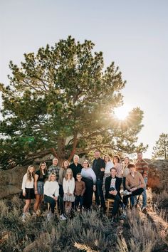 a large group of people posing for a photo in front of a tree with the sun behind them