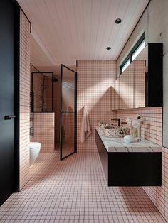 a bathroom with pink tiles and black fixtures, including a sink, toilet, and shower stall