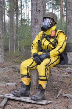 a man in yellow and black is sitting on a tree stump wearing a gas mask