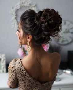 a woman with her hair in a low bun, wearing gold earrings and a lace dress