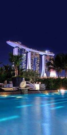 an outdoor swimming pool at night in front of the marina bay hotel and casino resort