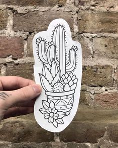 a hand holding up a sticker with an image of a cactus in a pot