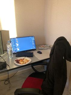 a laptop computer sitting on top of a desk next to a plate of food and water