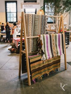 a wooden chair with blankets on it in a room filled with tables and people standing around