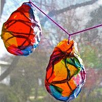 two colorful balls hanging from a string on a window sill in front of a tree