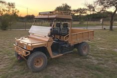 an orange utility vehicle parked in a field with trees and fence behind it at sunset